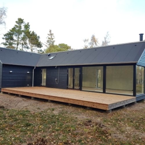 Tilbygning til hus med sort facade, store vinduespartier og træterrasse