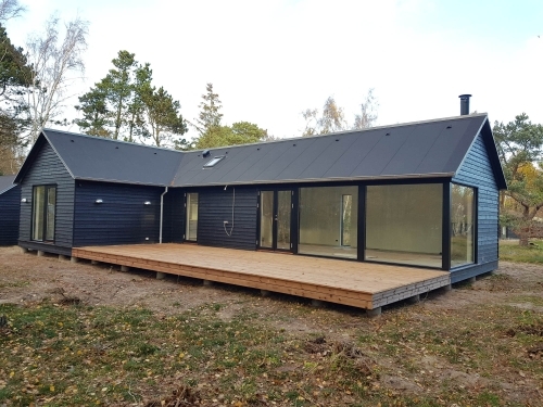 Tilbygning til hus med sort facade, store vinduespartier og træterrasse